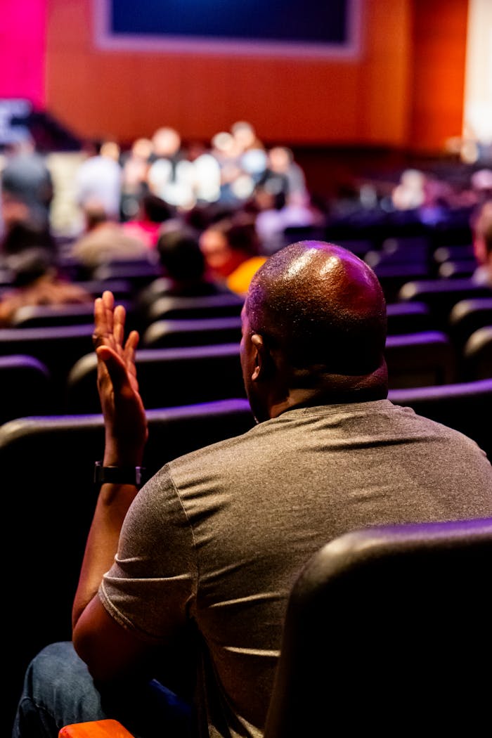 contact-img Man in auditorium engaged in a live presentation. Vibrant setting.