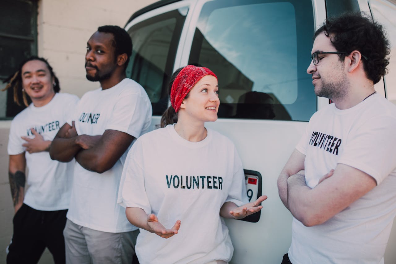 gallery-5 Four volunteers interacting by a van, promoting community service and involvement.