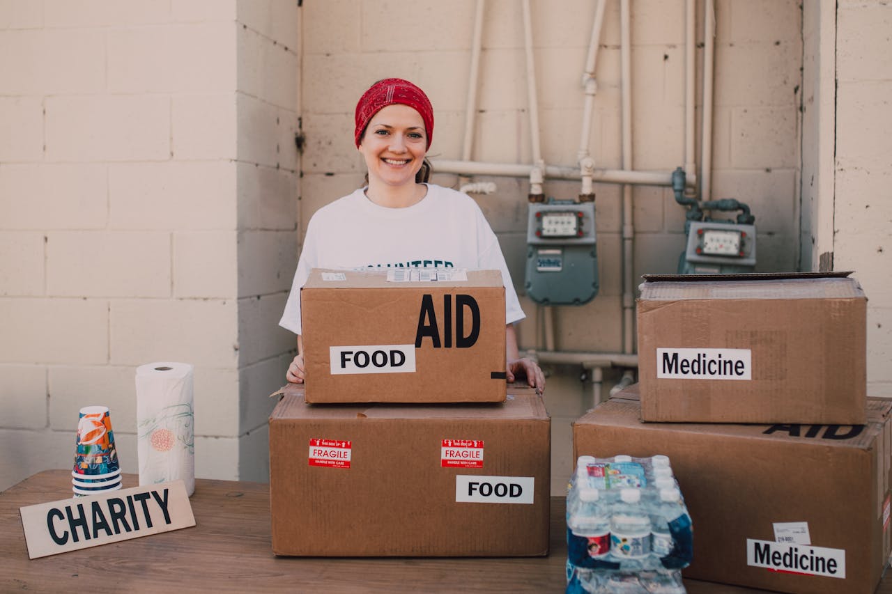 ours-journey Woman volunteer distributing aid packages with food and medicine for charity outdoors.